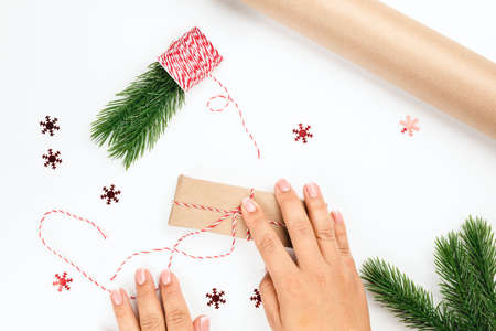 woman tie red and white rope on gift box with decor of Christmas tree branches and red snowflakes
