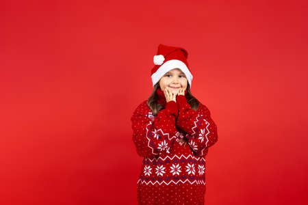 portrait of cute, Caucasian girl in red knitted Christmas sweater with reindeer holding palms to...