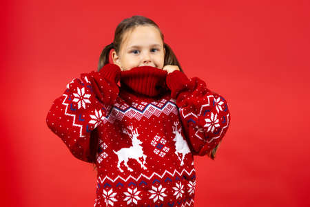 portrait of joyful girl wearing red Christmas sweater with reindeer , isolated on red backgroundの写真素材