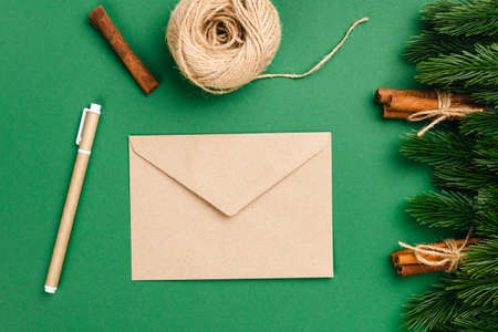 mockup of craft paper envelope and craft pen on green background with decorations of Christmas tree branches and cinnamon bundlesの写真素材