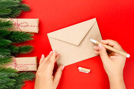 top view, process of writing letter to Santa Claus on craft envelope on red table with decorations from Christmas trees and gift boxesの写真素材