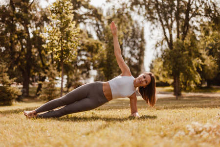 attractive, elegant woman do yoga and stand in side plank while maintaining balance on green grass of lawn at sunset, concept of inner harmonyの写真素材