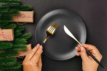 top view of woman hands holding knife and fork over empty black plate with frame of Christmas tree branchesの写真素材