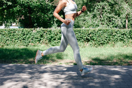 running fast attractive young sporty woman warming up, stretching in grey sportswear in park in sunny summer dayの写真素材