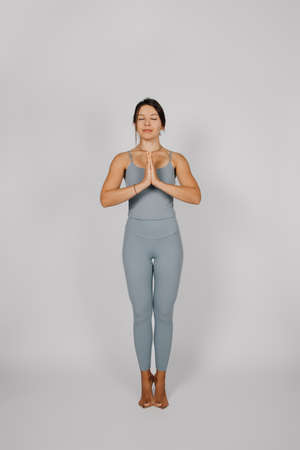 Woman is engaged in sports. Brunette in sports suit performs yoga exercise on isolated background,...
