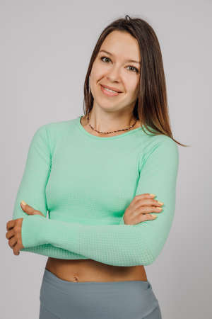 Beautiful brunette posing. Portrait of happy young woman in tracksuit for yoga or fitness posing in studio on gray isolated background, she crossed her arms and tilted her headの写真素材