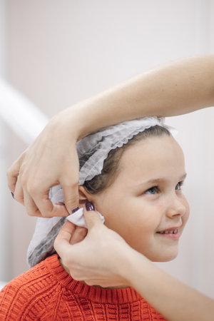 close-up of nurse hands wiping ears of little girl with antiseptic, alcohol or disinfectant,...