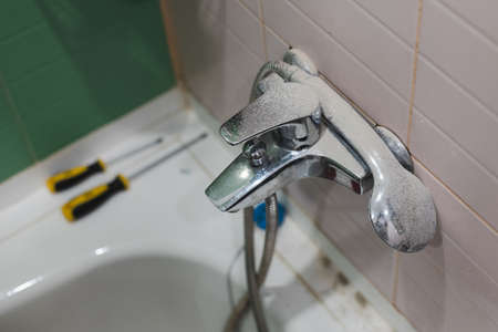 Dirt and dust on faucet and shower head because of renovation works in bathroom with bathtub and two screwdrivers on it in background. Renovation process causing dirtの写真素材