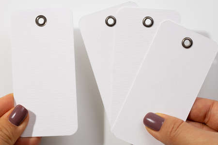 Female hands with four cardboard blank white colored tags of rectangle shape with tiny holes in...
