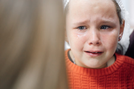 Portrait of little tearful girl in medical disposable cap crying in pain after ear piercing or other medical procedures in hospital officeの写真素材