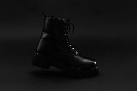 Side of isolated unisex leather autumn winter boot of black color on bright black background. Boots...