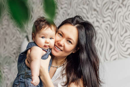 Portrait of smiling mother with little daughter in bedroom closeup, free copy space, blurred background. Have fun with cute baby, capture happy emotions. Concept of maternal affection and childcareの写真素材