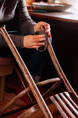Closeup of lady sitting sanding surface of aged stool in need of renovation with help of sandpaper in home workshop. Sustainable practices. Reuse of old things. Recycleの写真素材