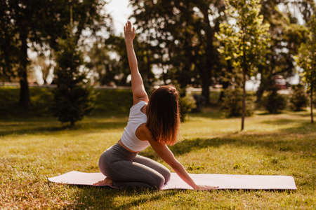 full length yoga concept. sporty slim woman with dark hair sit on her legs with raised left hand on...