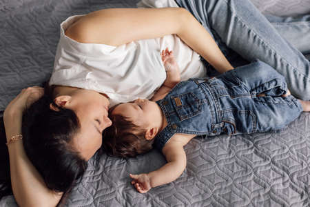 Portrait of young mother with little daughter in bedroom closeup, free copy space, gray background....