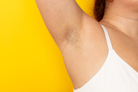 Woman touch hairy underarms with hand closeup, free copy space, yellow background. Raised arm with armpit hair. Female beauty trend, freedom, feminism, body positive, naturalness. Hygiene conceptの写真素材