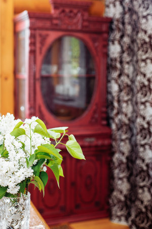 Old antique red wooden cupboard with carved decorations in corner of log hut near brown curtain with floral patterns.の写真素材