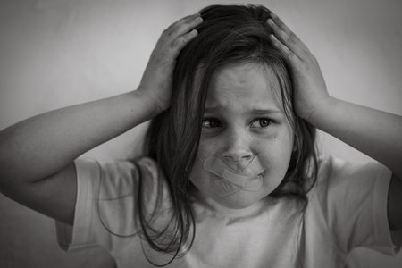 Black and white portrait of little panicked girl with long dark hair grabbing head. Mouth sealed...
