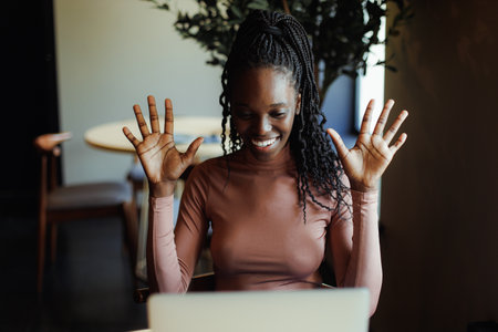 Joyful afro american woman emotionally talking gesturing on laptop online in coffee house. Black...