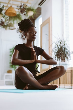 Vertical meditating bafrican american multicultural woman with namaste hands in yoga lotus position. Balanced lifestyleの写真素材