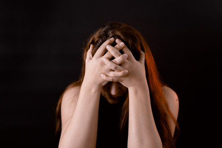 Woman with complexes put head down covering face with hands. Upset girl, introvert. Feelings, life difficulties.の写真素材