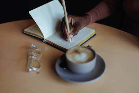 Cropped photo of African-American woman sitting at table with cup of coffee, glasses in cafe, taking...
