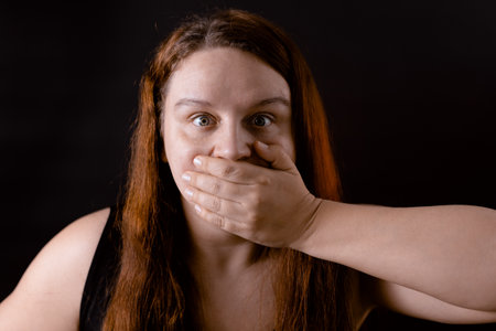 Restless young woman closing mouth with hand. Indignant girl suffering. Deprive of freedom of speech, keep mouth shut.の写真素材