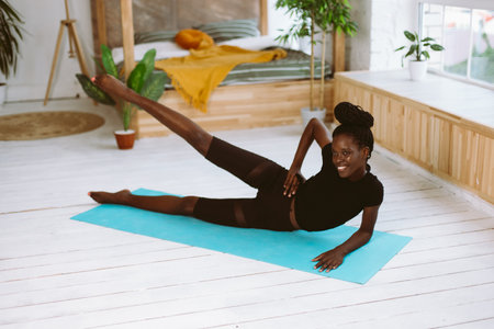 Beautiful athletic afro american woman lying on side and raising leg up, training on gymnastic mat in decorated photo studio. Sports course, exercise technique, fitness, keeping body fitの写真素材