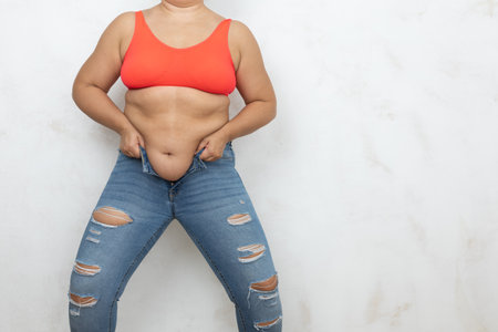Unrecognizable adipose, fat, obese and overweight woman in red bikini pull and getting dressed in small size tight jeansの写真素材