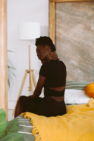 Beautiful afro american woman stretching neck muscles back view closeup, training and doing yoga in decorated studio. Muscle stretching, gymnastic exercises, fitness, keeping body fitの写真素材