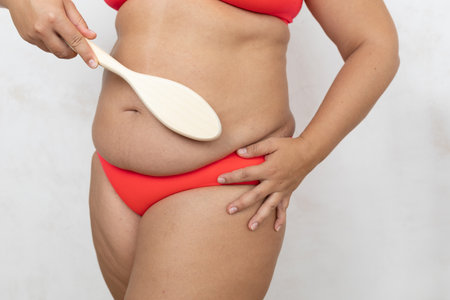 Cropped overweight fat female in bikini scrub belly use brush with natural bristles, dry massage for healthy beauty bodyの写真素材