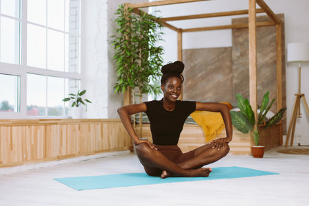 Beautiful and athletic afro american woman with smile sitting in butterfly pose, doing yoga on...