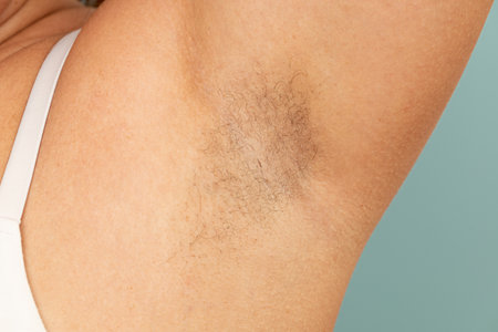 Woman touch hairy underarms with hand closeup, free copy space, yellow background. Raised arm with armpit hair. Female beauty trend, freedom, feminism, body positive, naturalness. Hygiene conceptの写真素材