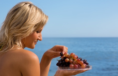 Attractive girl eating grapes at the beach by the sea.の写真素材