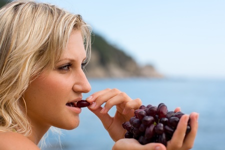Young woman eating grapes at the beach by the sea.の写真素材