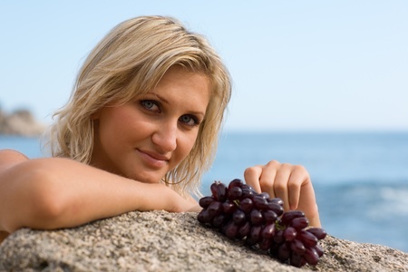 Beautiful girl and grapes at the beach by the sea.の写真素材