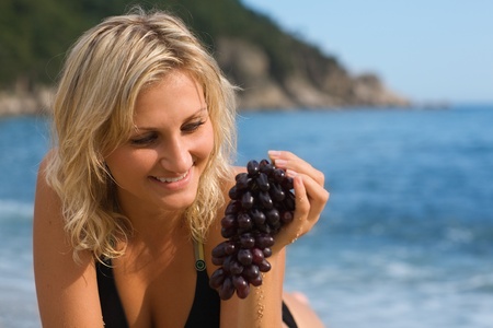 Beautiful girl with grapes on the beach by the seaの写真素材