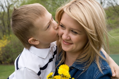 Son kisses mother. In his hand the boy flower dandelion.の写真素材