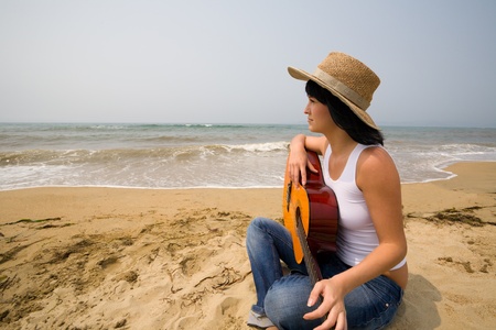 The girl holds a guitar and looks at the sea.の写真素材