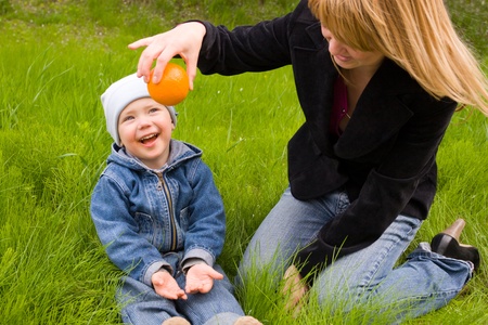 Mom and the son play with an orange on a lawnの写真素材