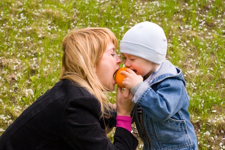 Mom and the son play with an orange on a lawn.の写真素材