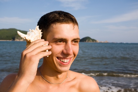 The young man holds a shell in a hand.Sea coast.