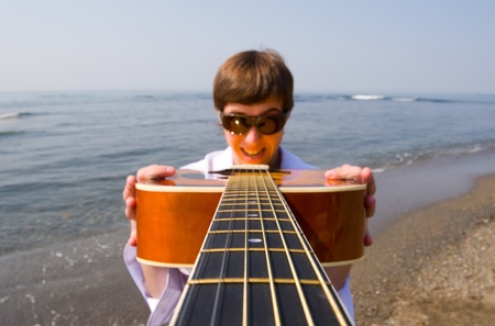 Young man (musician) holds a guitar in hands.Coast.