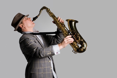 Young man playing the saxophone on a gray background.の写真素材