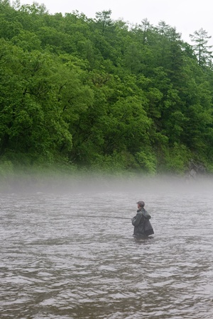 Fisherman catches of salmon on a mountain river. Is rain. Fog.の写真素材