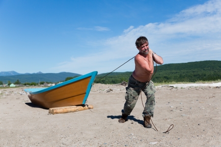 Fisherman pulls a heavy wooden boat out to sea. Humor.の写真素材