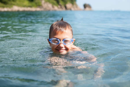 Joyful boy swims in the sea with glasses for swimming の写真素材