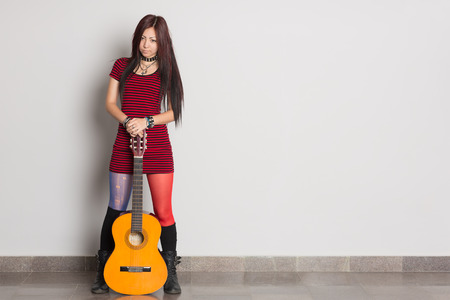 Beautiful young Asian girl with a guitar standing at the wall.