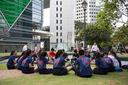 SINGAPORE - FEBRUARY 18, 2015: Boys and girls sitting on the lawn in downtown Singapore and discuss their urgent  affairs.のeditorial素材