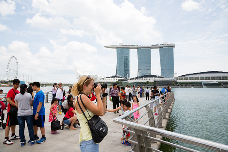 SINGAPORE - FEBRUARY 18, 2015: Tourists take pictures near the Merlion sculpture in the background of Singapore. In the background is the famous hotel and casino Marina Bay Sands.のeditorial素材